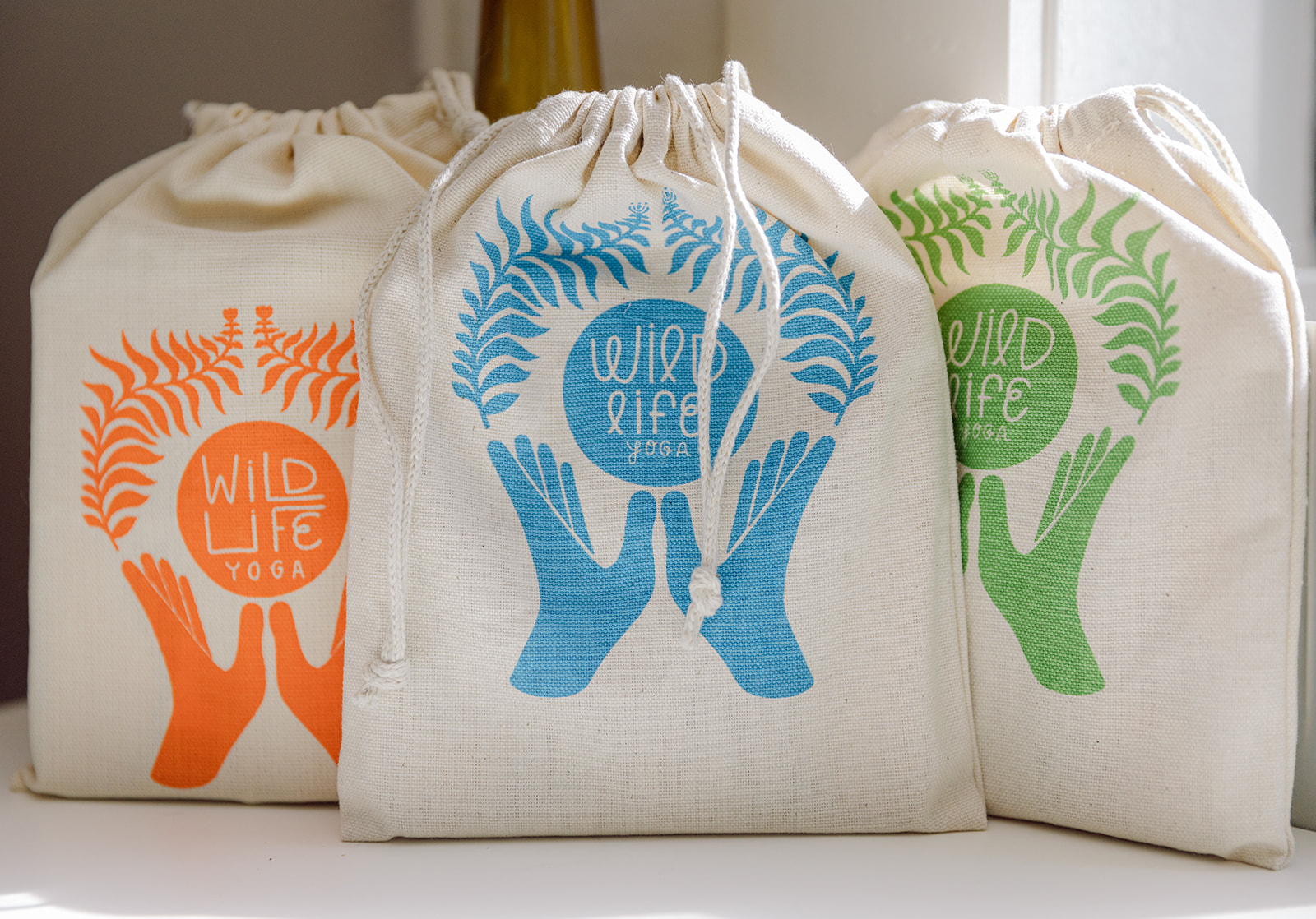 three sets of bags of cards lined up with each other to display the cards. the logo for wild life yoga is on each of them. there is an orange, blue and green bag. 