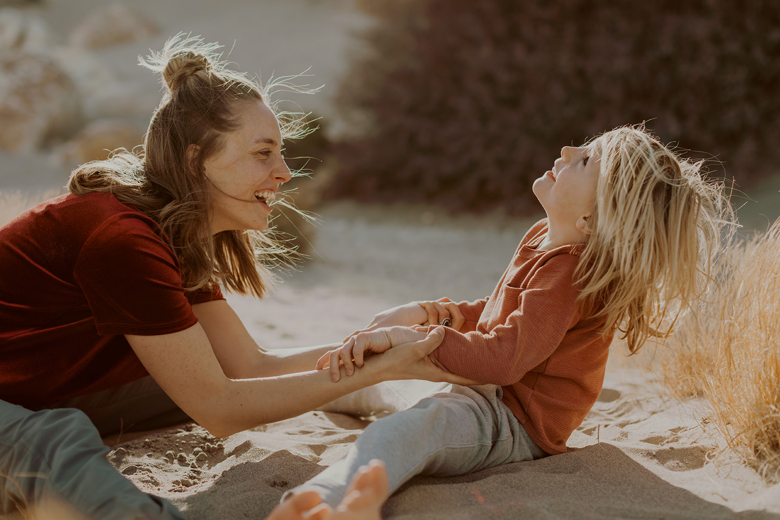 A mother and child holding hands in a wide leg forward role. their legs are together and they are laughing while hinging back and forth. 