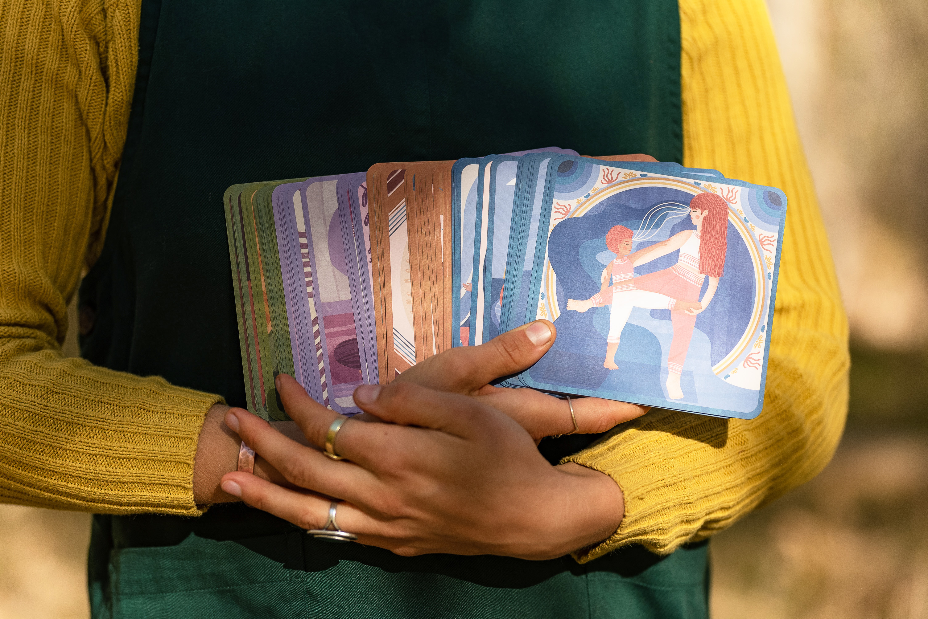 person holding a deck of 5x5 inch cards in each of the elelemtnal colors: blue for water, orange for earth, purple for air, and green for earth. there are 52 cards held. 