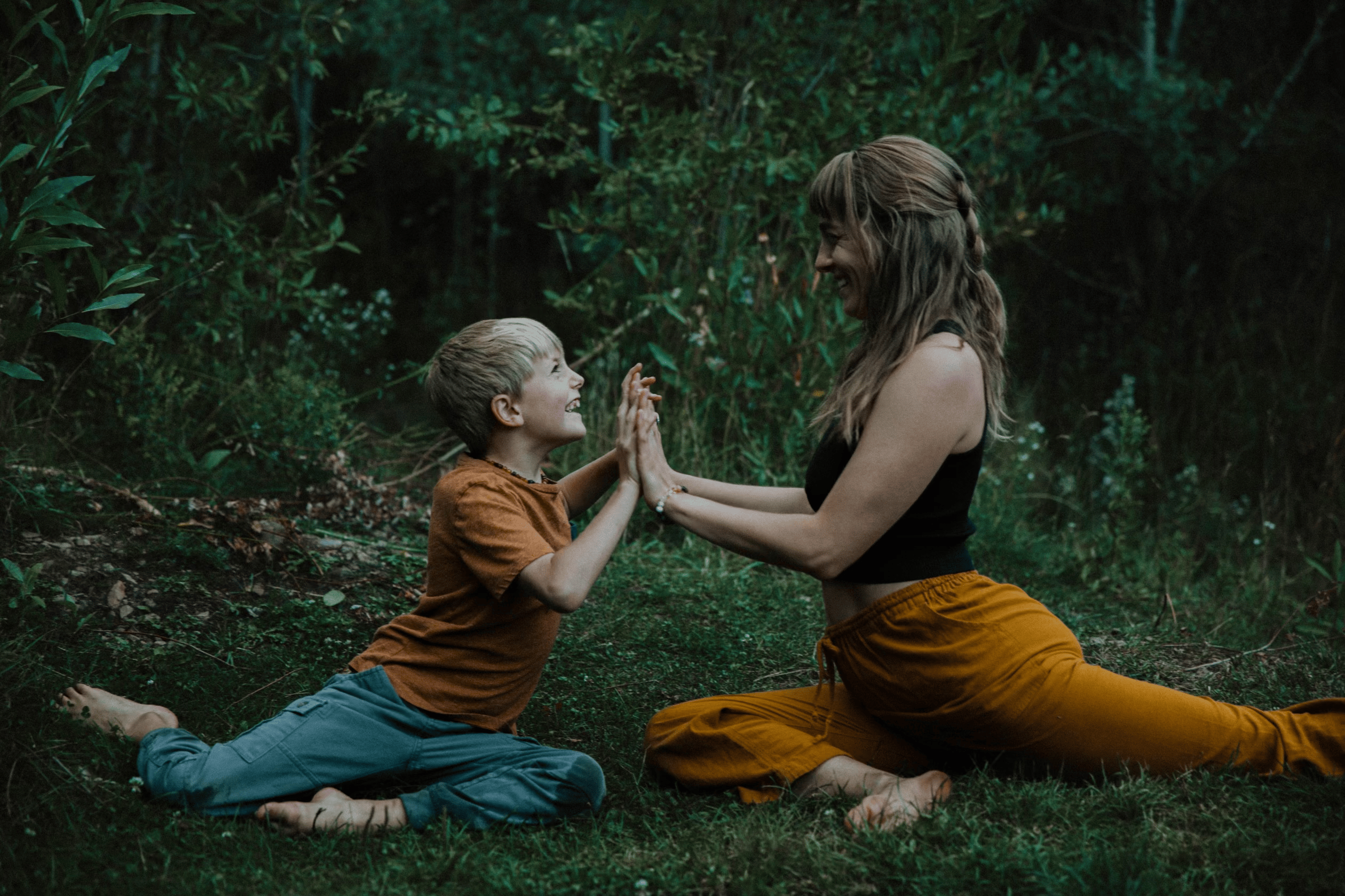Mother and son doing yoga together in pigeon pose with their hands pressed together out in nature